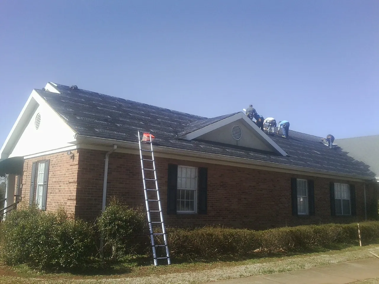 Crew tearing shingles off a brick ranch roof with a ladder set — Metal Roof Repair work by our crew in Silver Springs